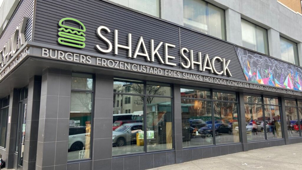 Shake Shack store exterior with customers enjoying delicious burgers.